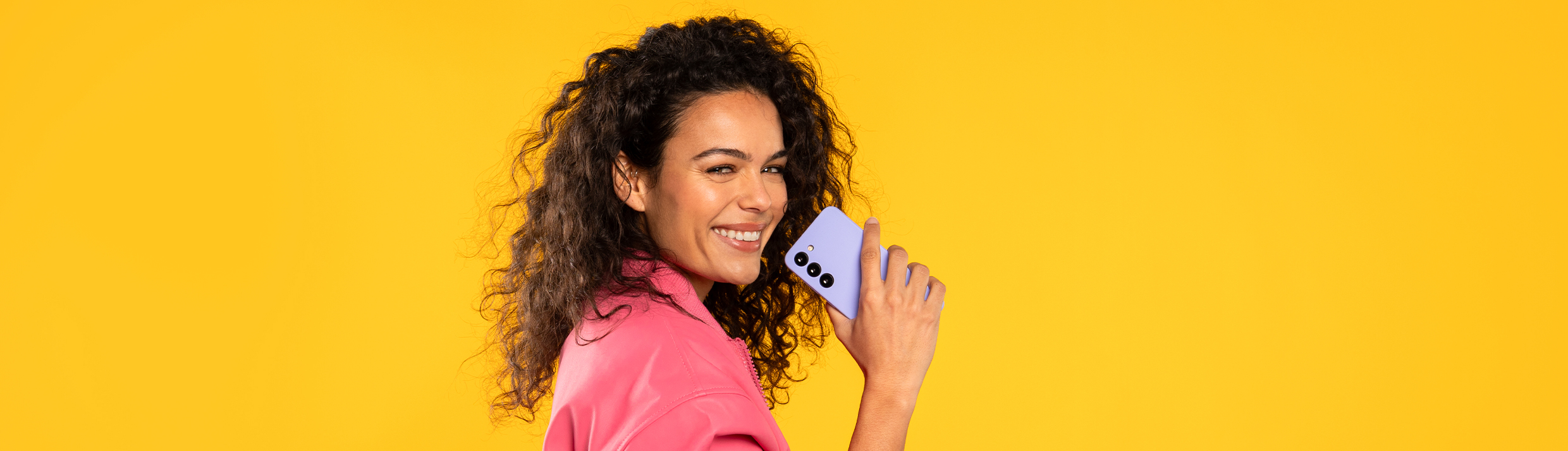 Une femme souriante tient une coque de téléphone violette, l'arrière-plan est jaune.