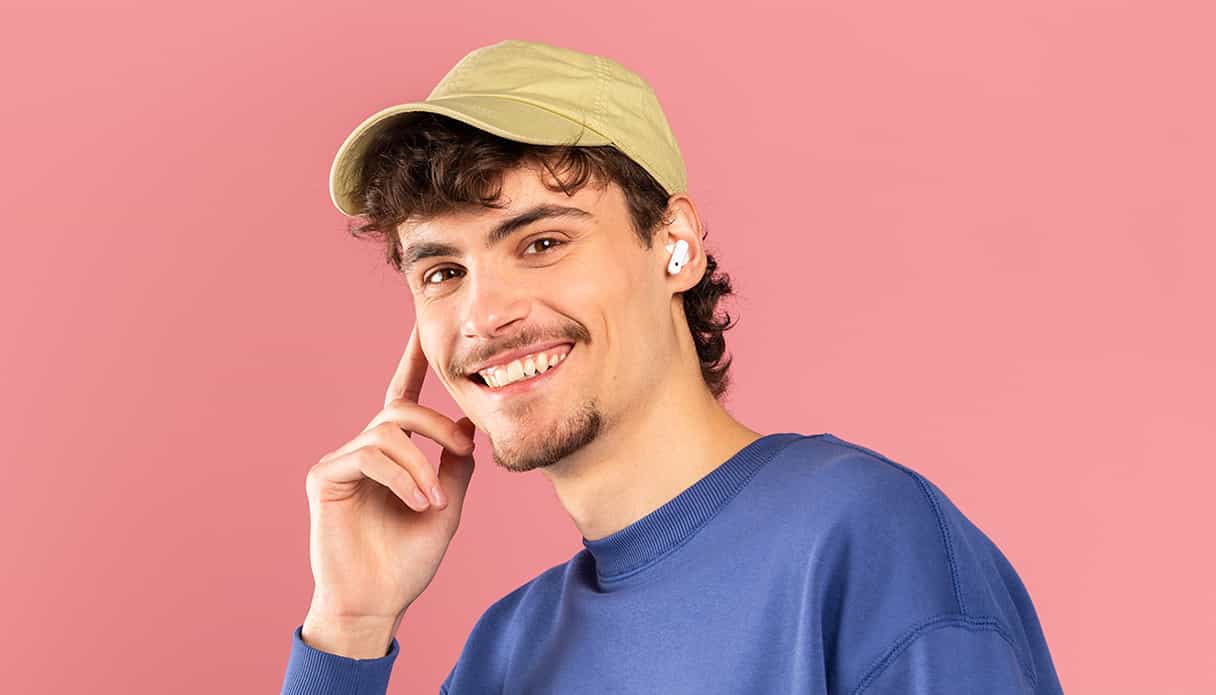 Un modèle masculin avec une casquette sur la tête affiche un grand sourire et porte des AirPods sans fil.