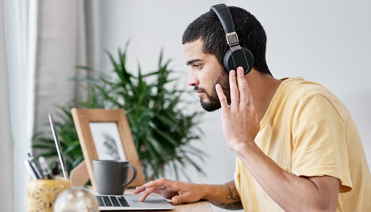 Un homme est assis à son bureau, regardant son ordinateur portable, tout en portant un casque avec réduction de bruit.