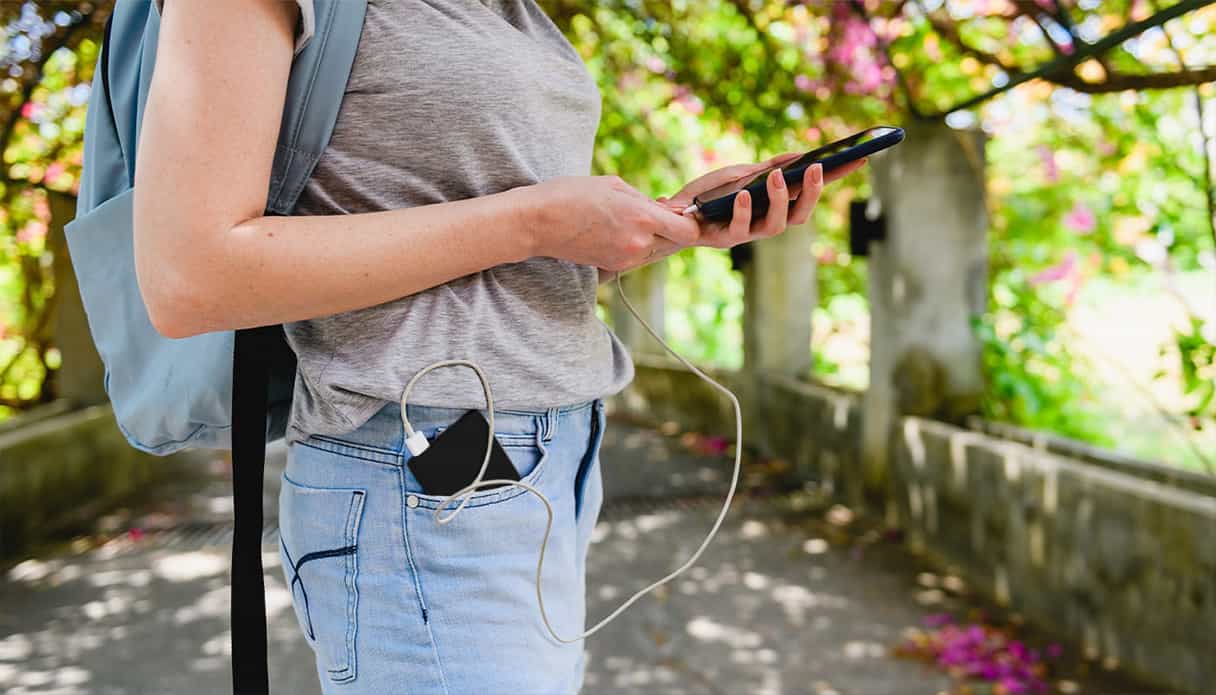 Femme au parc, téléphone en main, batterie dans poche, connectée.