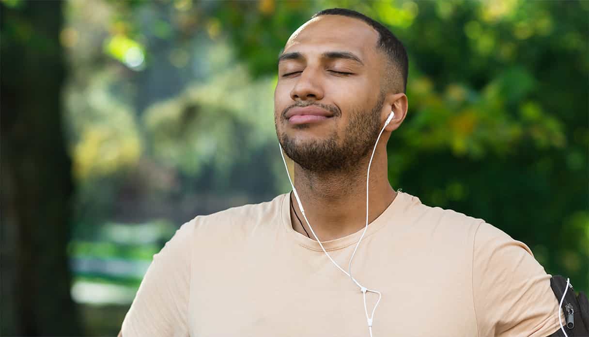 L'homme respire profondément, écoutant sa musique avec des écouteurs filaires dans le parc.