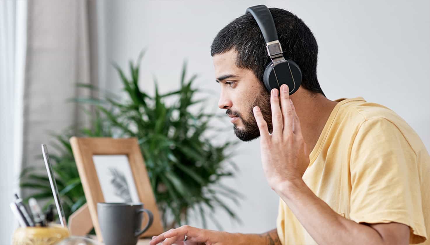 Un homme est assis à son bureau, regardant son ordinateur portable, tout en portant un casque avec réduction de bruit.