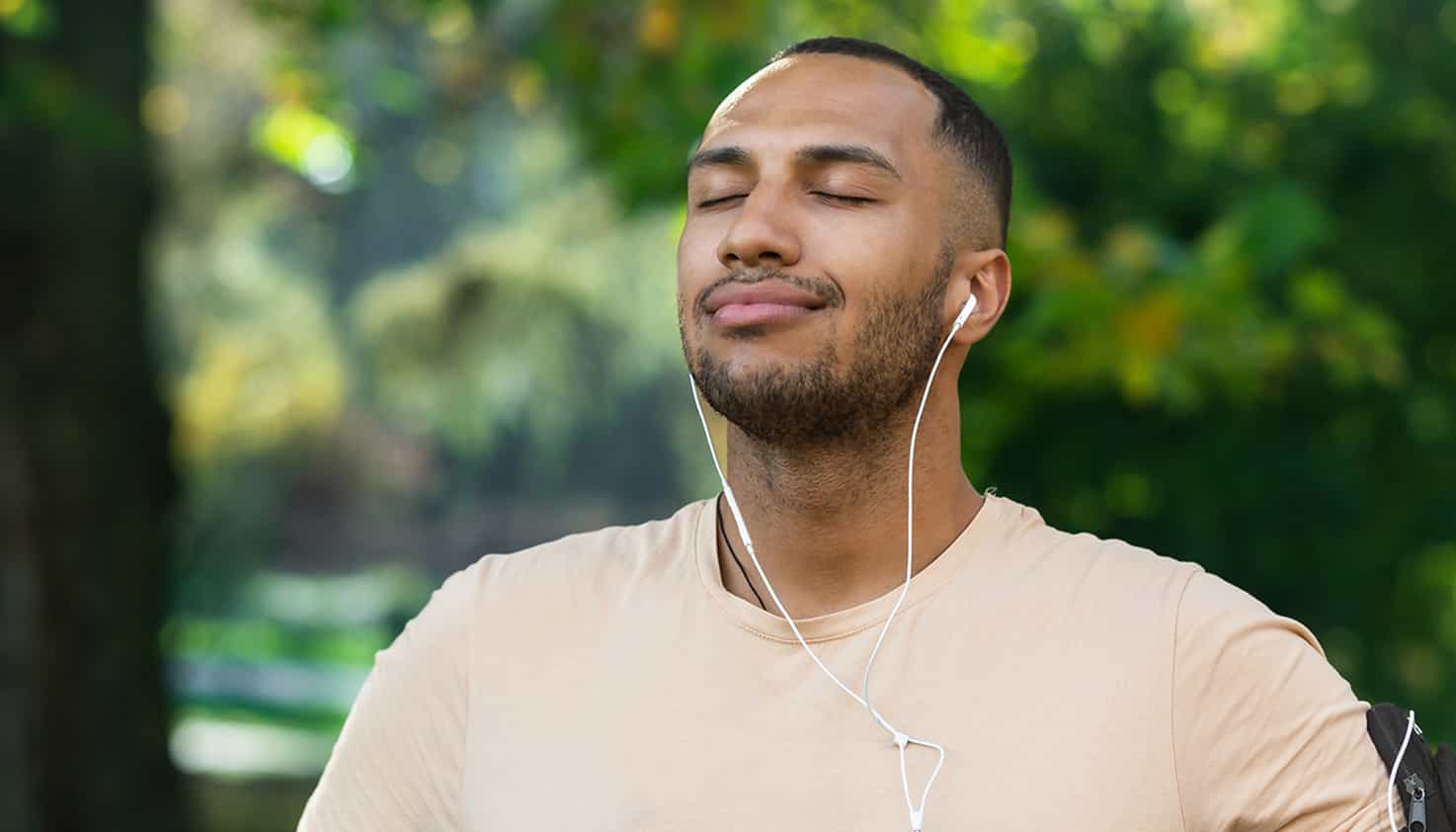 L'homme respire profondément, écoutant sa musique avec des écouteurs filaires dans le parc.