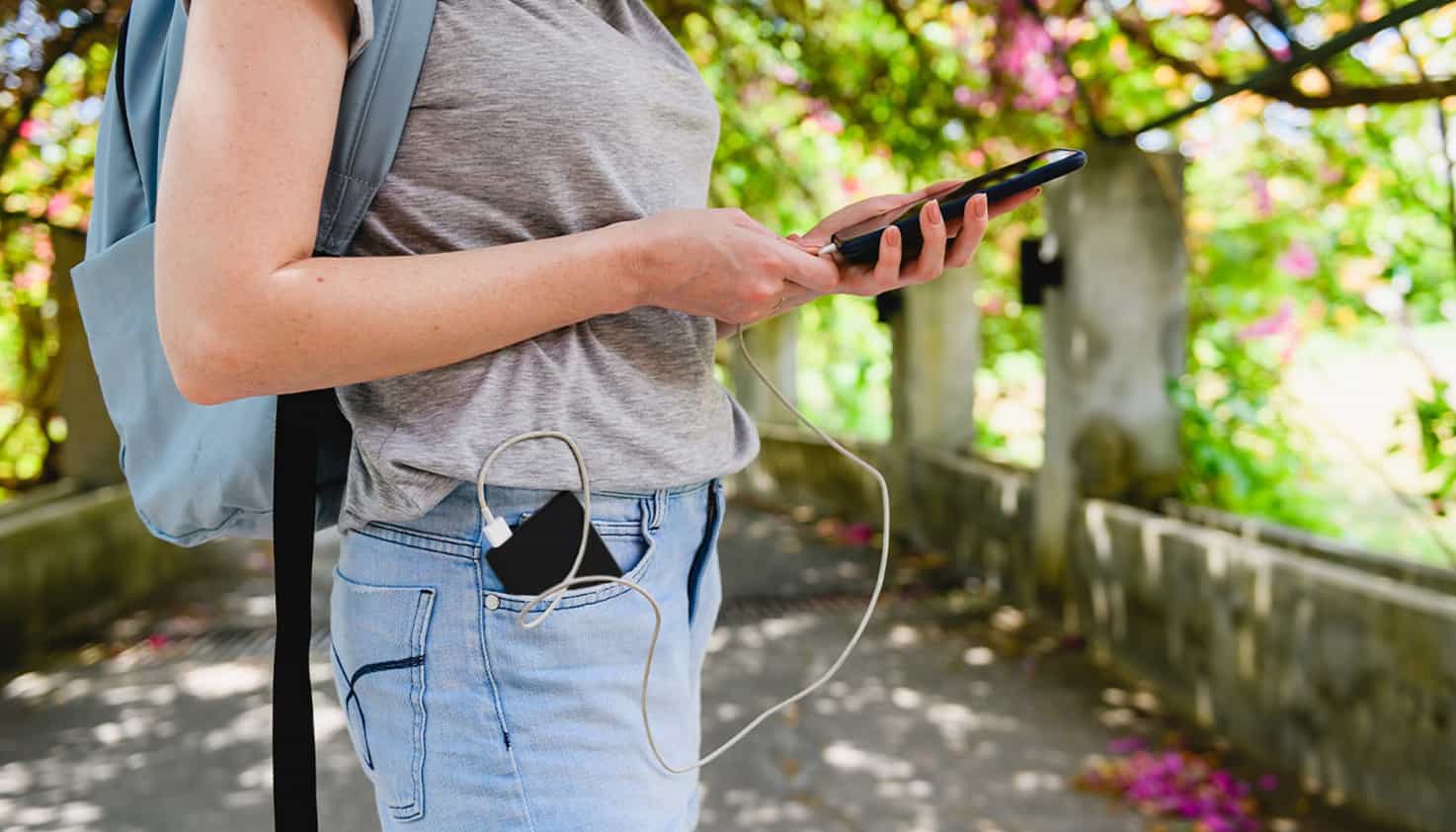 Femme au parc, téléphone en main, batterie dans poche, connectée.