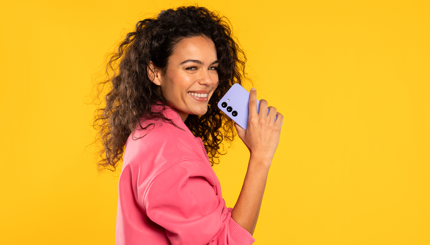 Une femme souriante tient une coque de téléphone violette, l'arrière-plan est jaune.