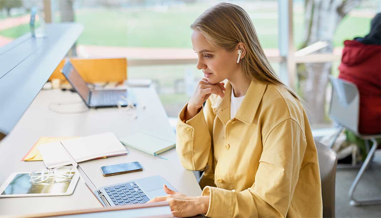 Une femme travaille à un bureau sans être dérangée par son environnement grâce à des écouteurs à réduction de bruit.