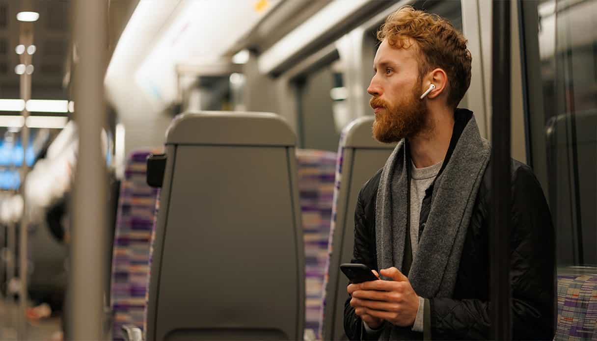 Un homme est assis dans le train, écoutant son podcast avec ses écouteurs.